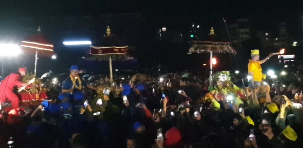 Dyah Lwākegu: Meeting of three sisters at Tundikhel Palanquin of three sisters, Kanga Ajima (red), Wotu Bhadrakali (blue), and Tebahal Ajima (yellow) amidst the community at Tundikhel.